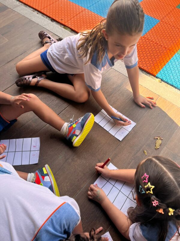 Grupo de crianças interagindo e fazendo atividade escolar de forma descontraída, promovendo o desenvolvimento social e o trabalho em grupo.